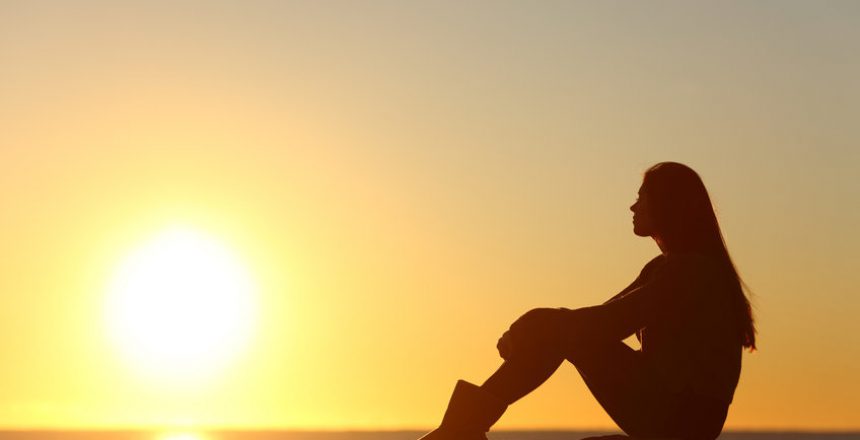 Profile of a woman silhouette watching sun on the beach at sunset